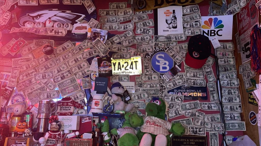 A photograph of a bar wall covered in dollar bills.