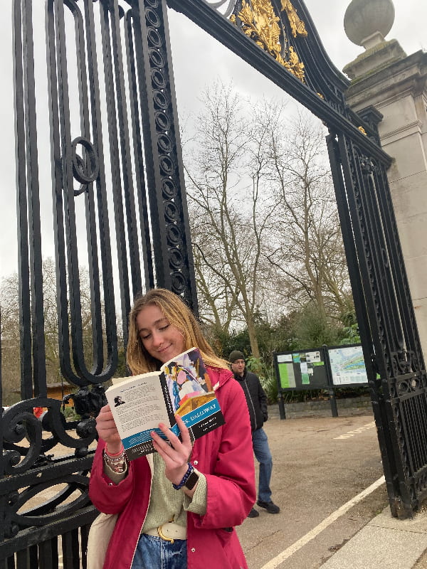 A young woman reads Mrs. Dalloway while leaning against the park gates